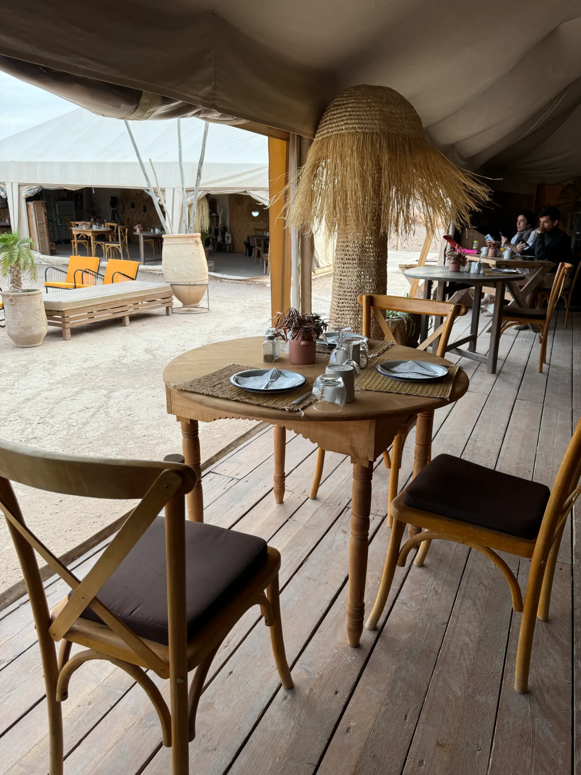 Open-air tented dining area with wooden tables and woven lamps in Morocco
