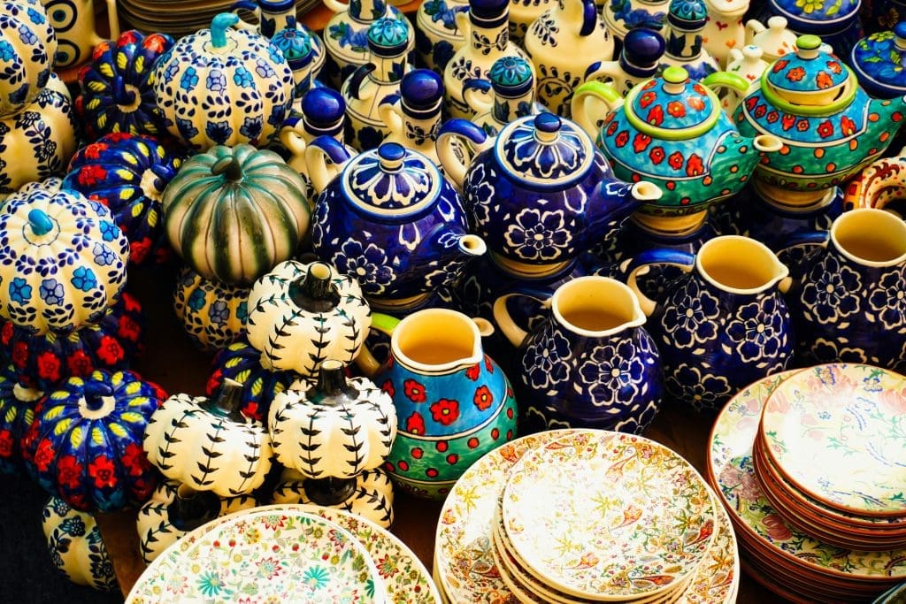 A display of colorful ceramic teapots, cups, pitchers, and plates with various floral and geometric patterns arranged closely together.